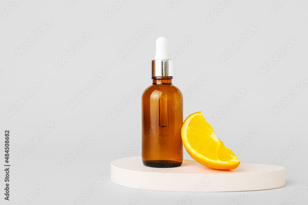 Bottle of essential oil and fresh orange on light background