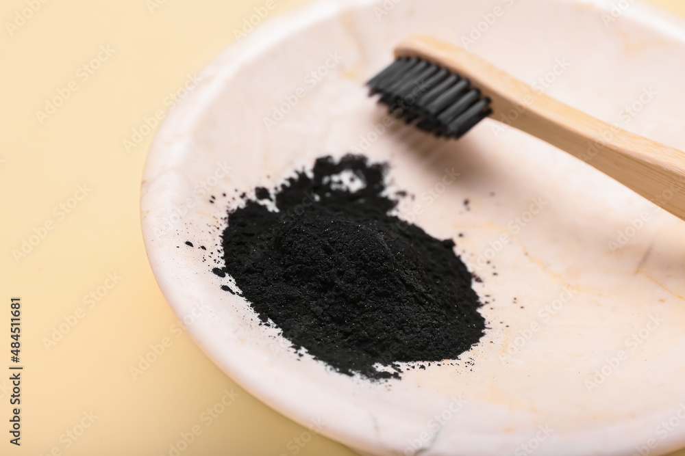 Plate with activated charcoal tooth powder and toothbrush on beige background, closeup