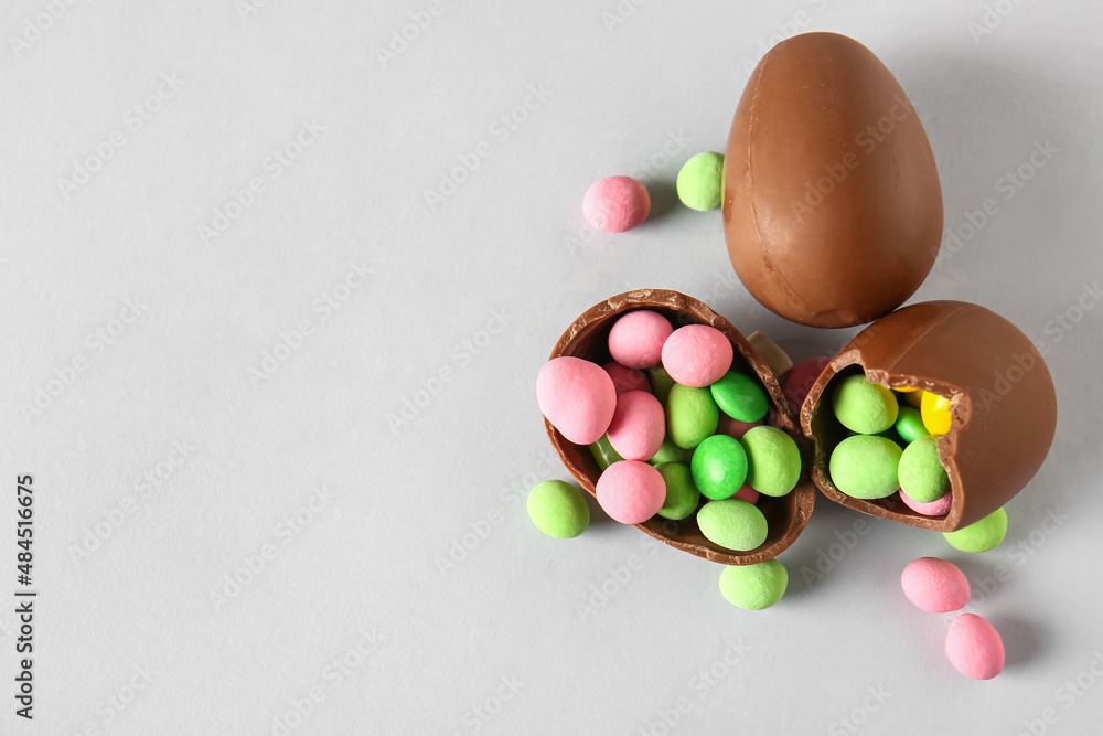 Broken chocolate Easter eggs with different candies on light background