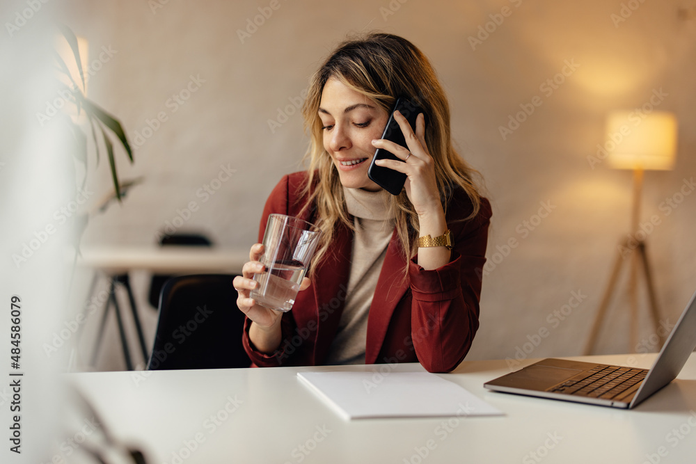 女商人拿着一杯水打电话。