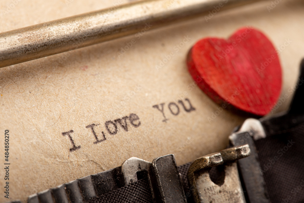 I love you - phrase on typewriter. Valentines Day greetings concept. Little red wooden heart close u