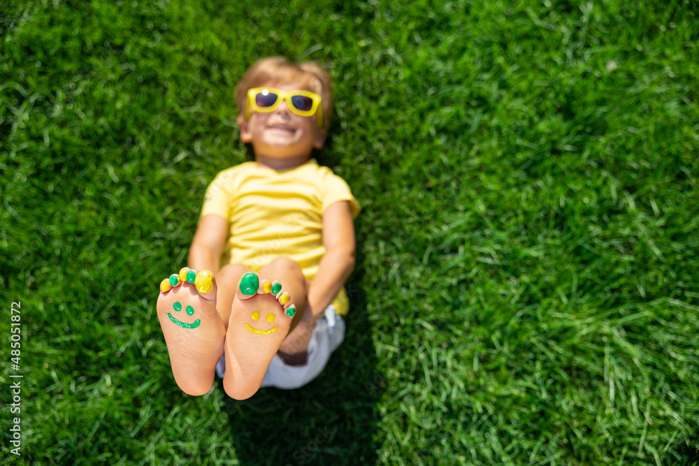 Happy child with smile on feet lying on green spring grass