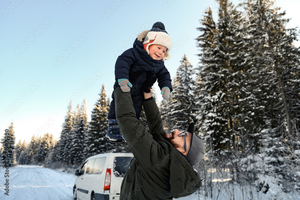 a father with a beard and glasses holds his little son in his arms on a winter walk against the back