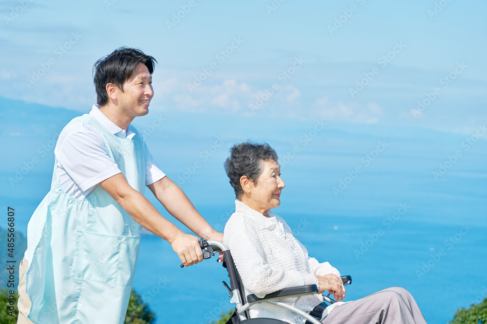 介護士と車椅子に乗る高齢者　屋外