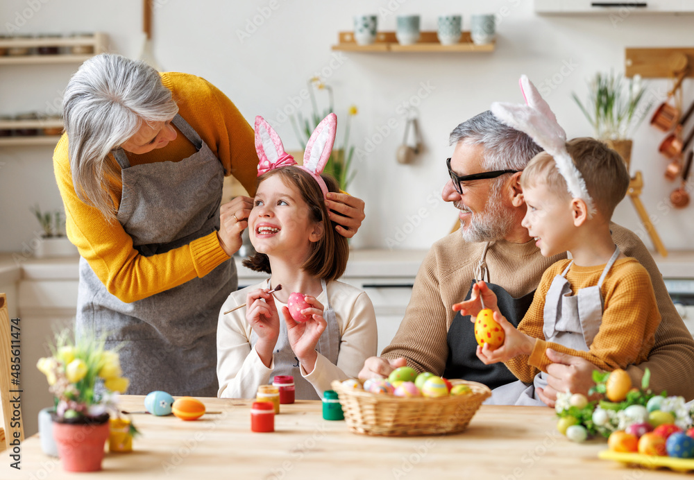 Happy family grandparents and kids enjoying Easter preparation together, coloring eggs in kitchen