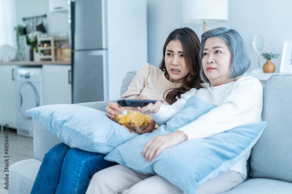 Asian old mature woman and daughter sitting on sofa watch scary movie. 