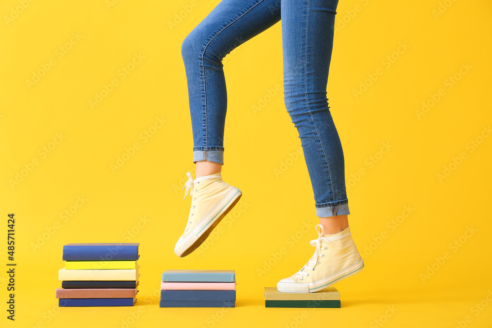 Creative composition with books and female legs on yellow background