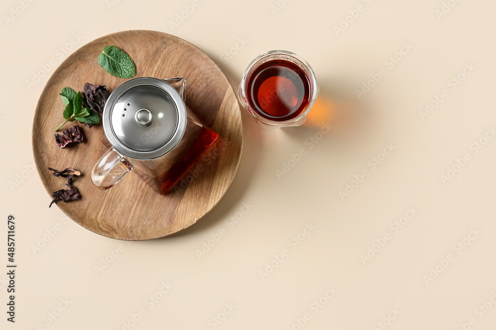 Teapot and glass of tasty tea on yellow background