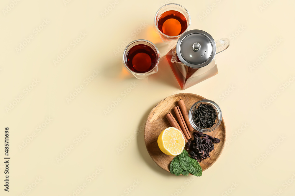 Composition of teapot, glasses with tasty tea and spices on yellow background