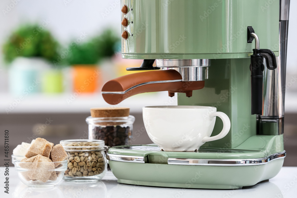 Modern machine with cup of fresh coffee on table in kitchen