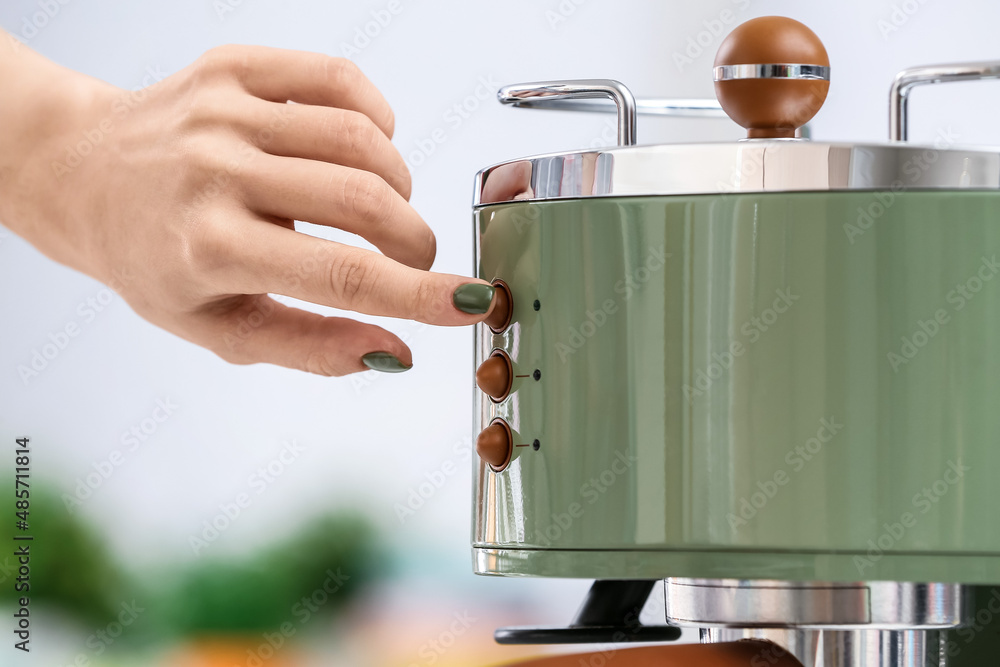 Woman turning on coffee machine in kitchen, closeup