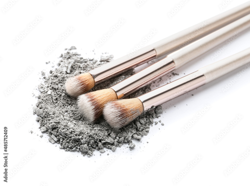 Makeup brushes and loose eye shadow on white background