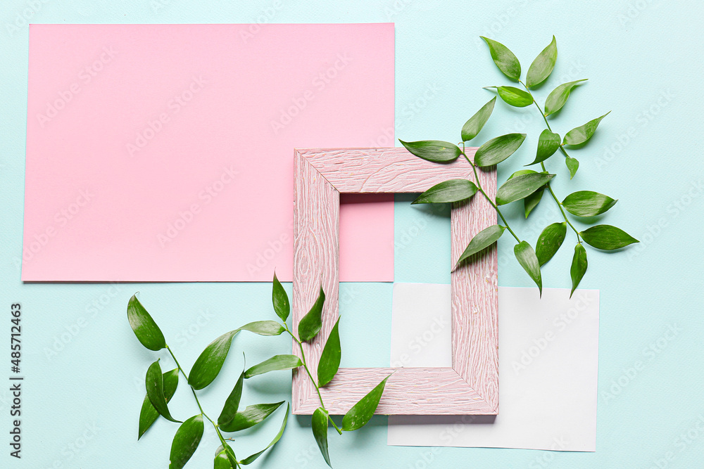 Composition with empty picture frame, blank cards and plant branches on color background