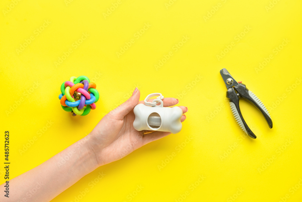 Female hand with pet waste bags, nail clipper and toy on yellow background