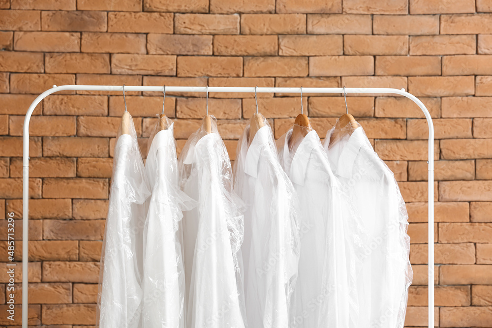 Rack with clean shirts in plastic bags near brick wall