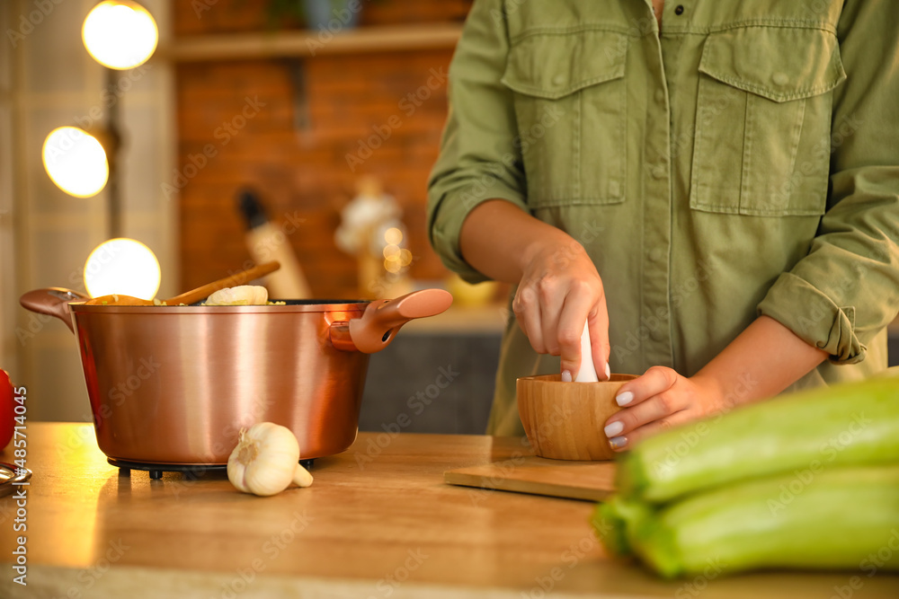 Woman grinding spices in wooden mortar and cooking pot with pilaf on table in kitchen