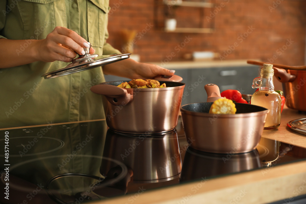 Woman holding cooking pot with vegetable stew and opening lid in kitchen