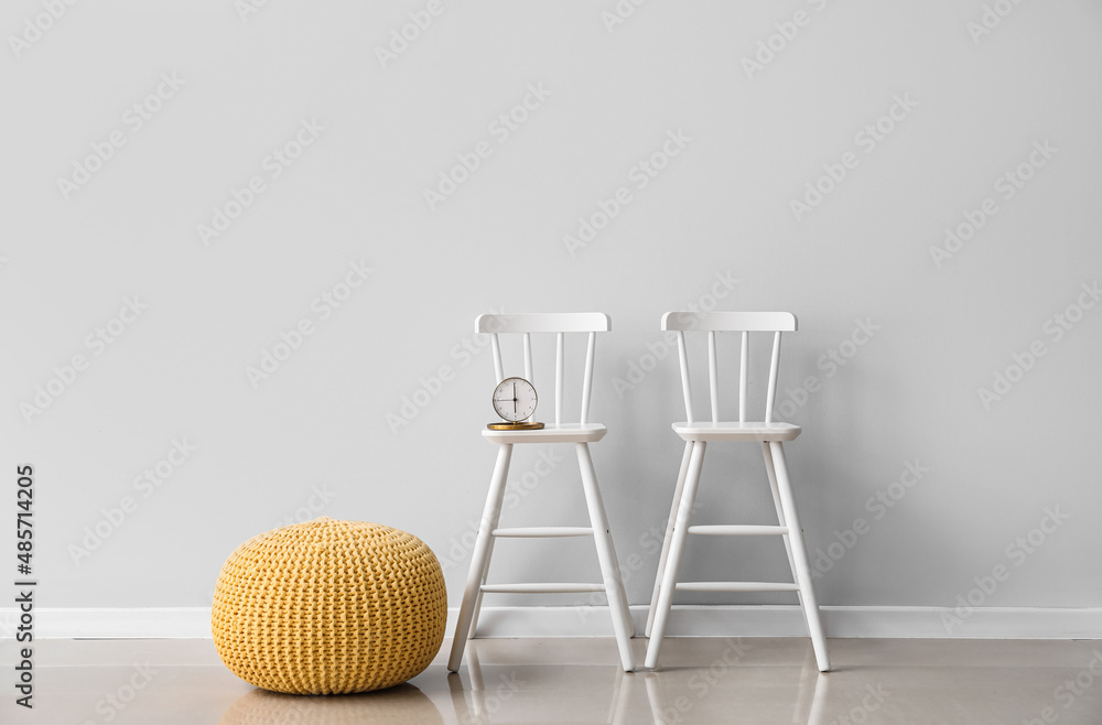 Comfortable pouf and chairs with alarm clock near light wall