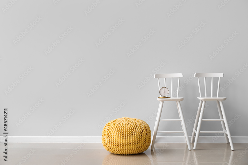 Pouf and chairs with alarm clock near light wall