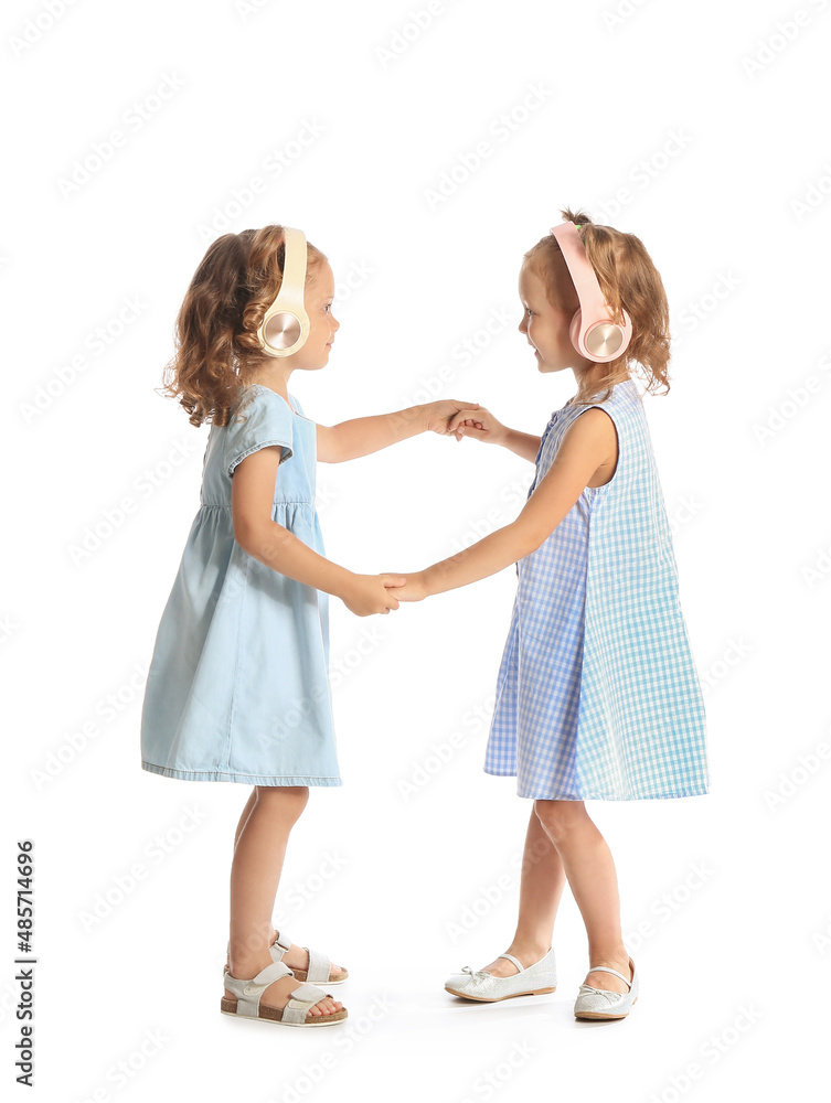 Adorable little sisters in headphones dancing on white background