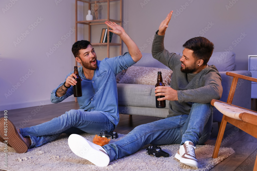 Young brothers with bottles of beer giving each other high-five at home in evening