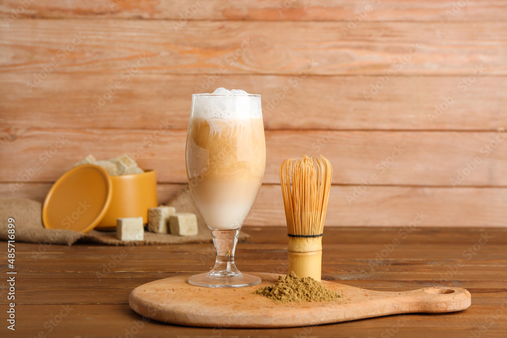 Glass of iced hojicha latte, chasen and powder on wooden table