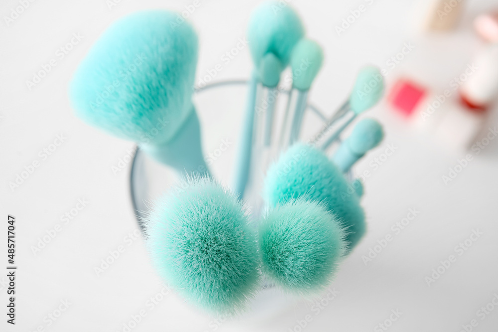 Glass with set of makeup brushes on light background, closeup