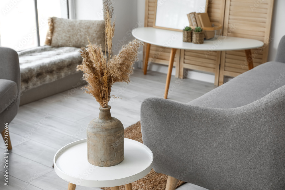 Vase with pampas grass on coffee table near sofa in light living room