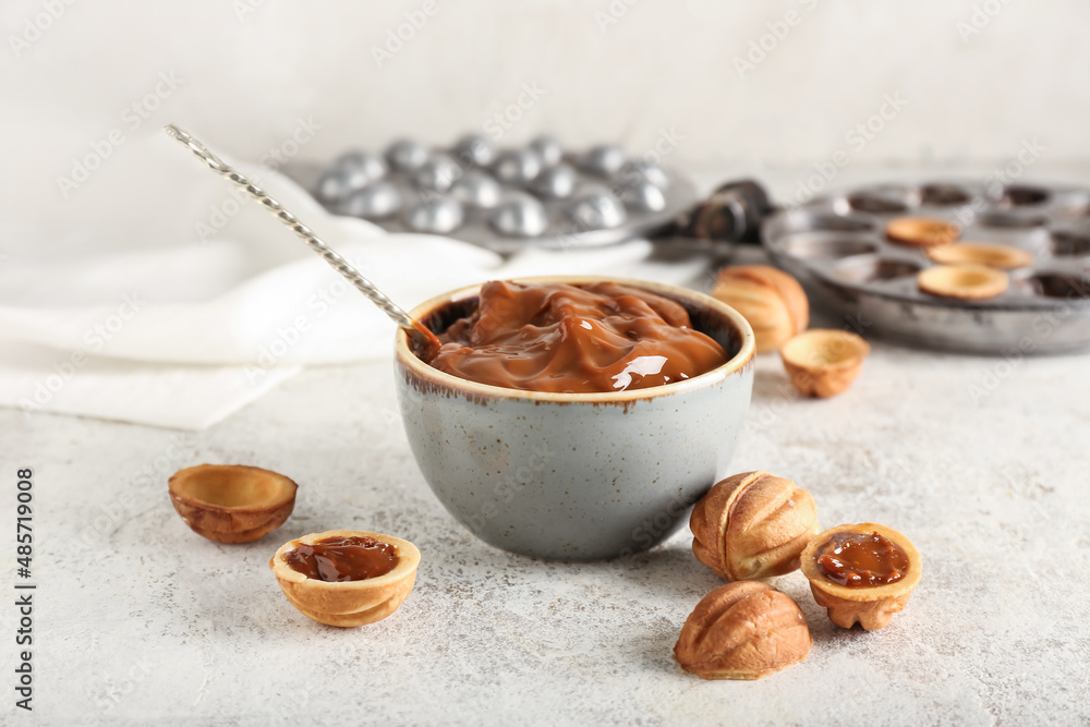 Bowl with boiled condensed milk and walnut shaped cookies on light background