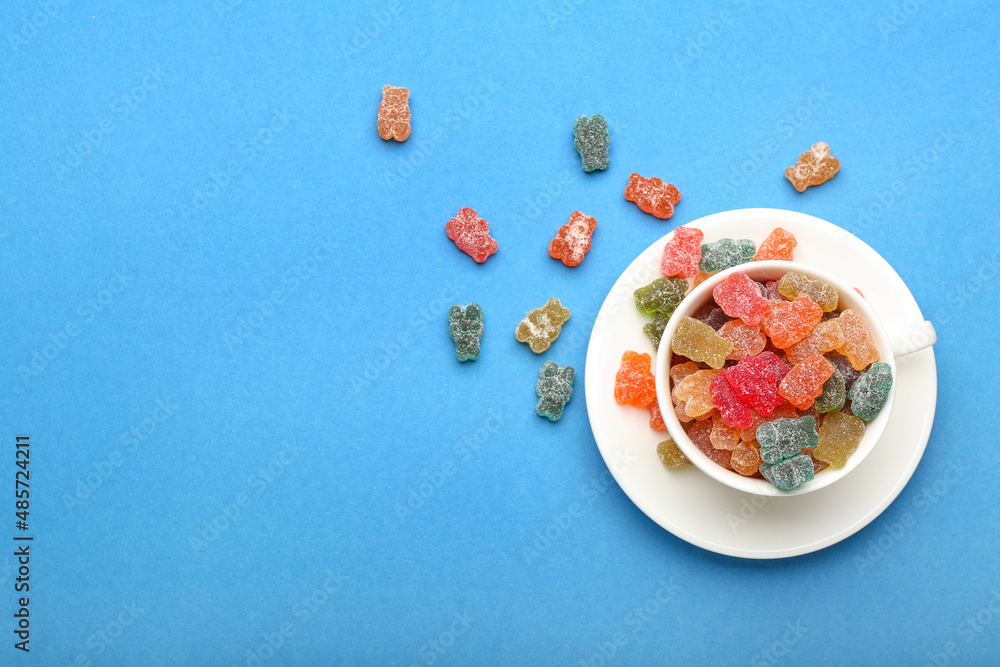 Cup with different jelly bears on color background