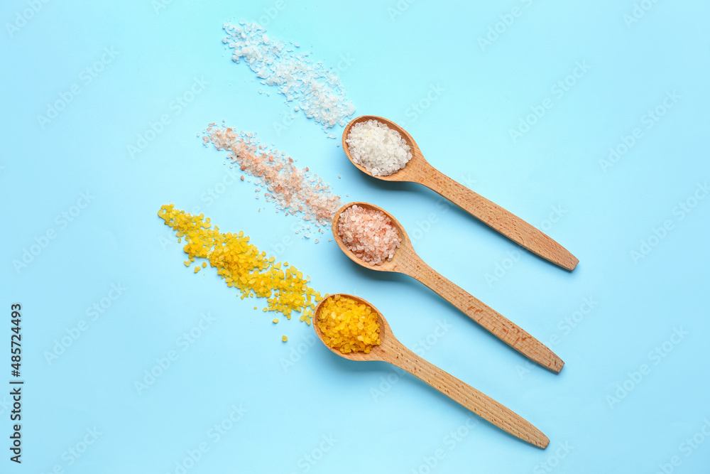 Wooden spoons with different sea salt on color background