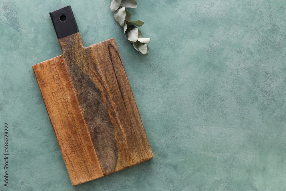 Wooden cutting board and eucalyptus branch on green background