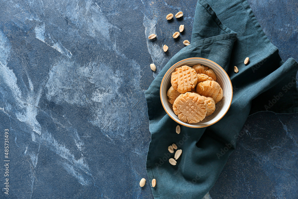 Bowl with tasty peanut cookies on blue background