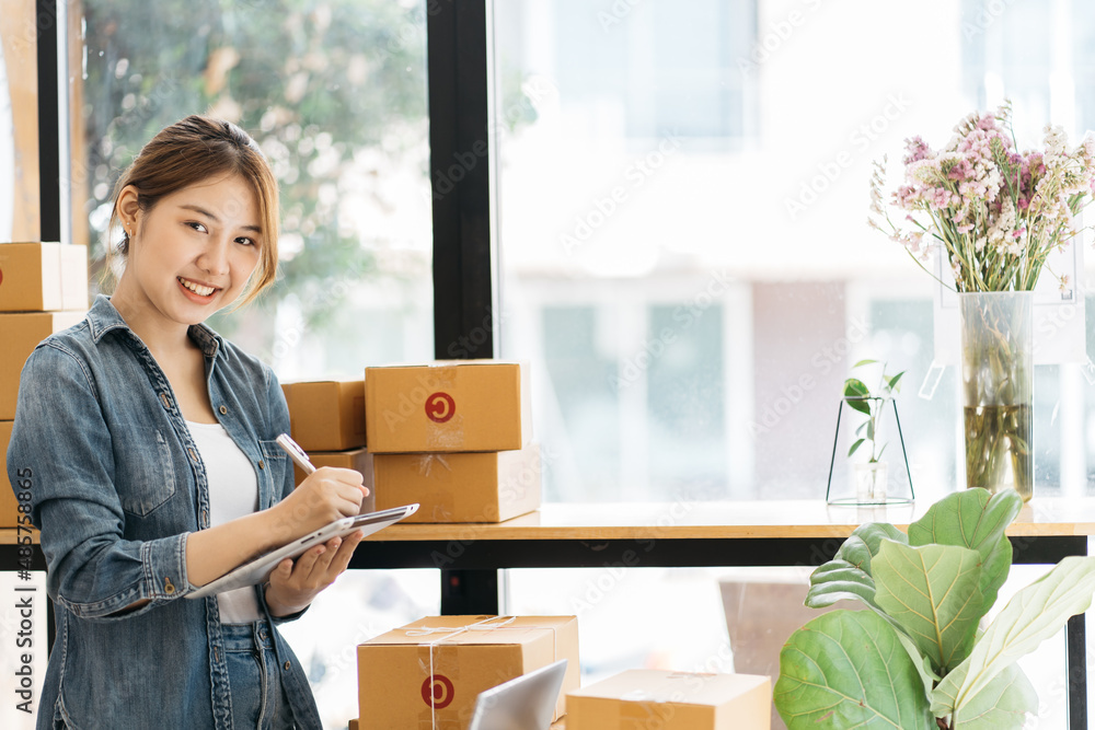 一位女士正在包装她在网上销售的商品。年轻的创业小企业主正在包装纸板箱