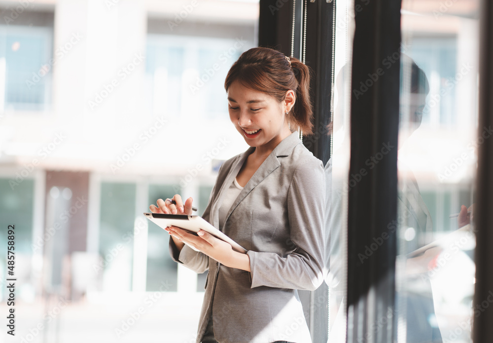 迷人的女商人站在办公楼的窗户前使用数字平板电脑