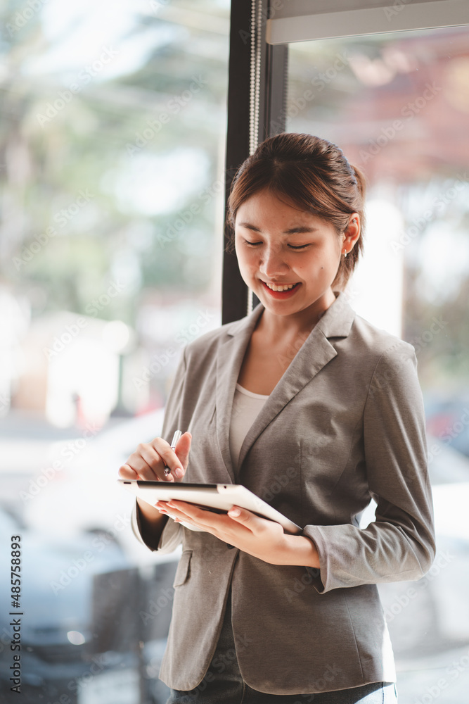 Attractive businesswoman using a digital tablet while standing in front of windows in an office buil