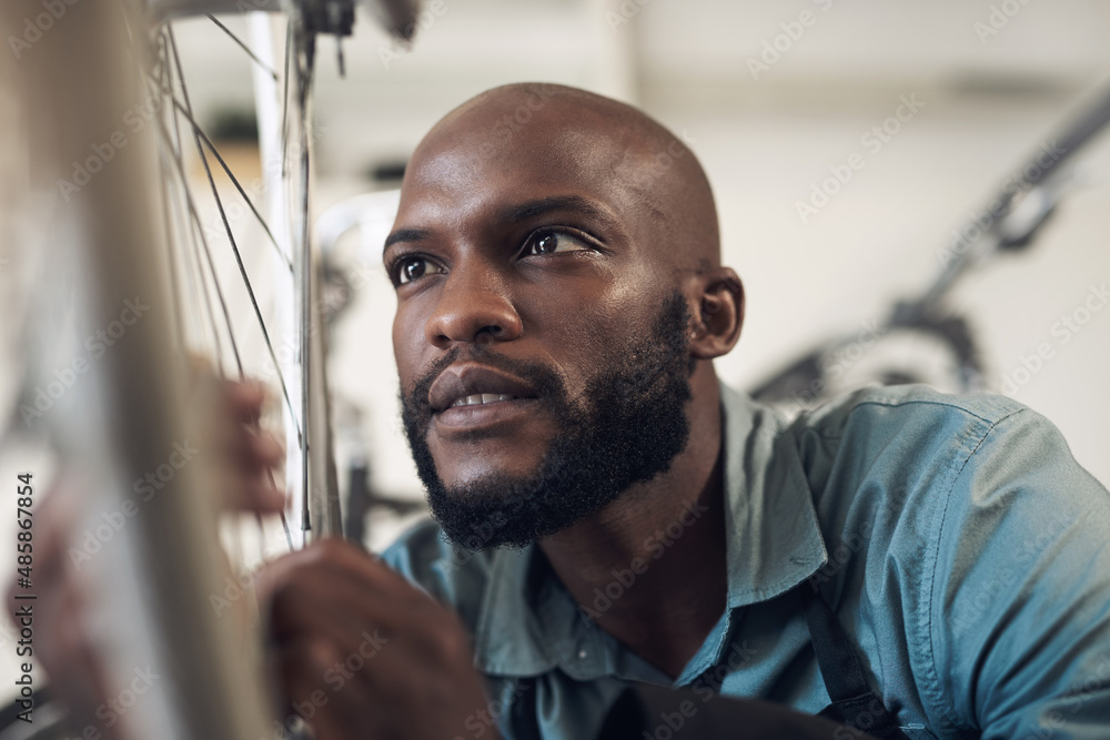 Whys it still crooked. Shot of a handsome young man crouching in his shop and repairing a bicycle wh