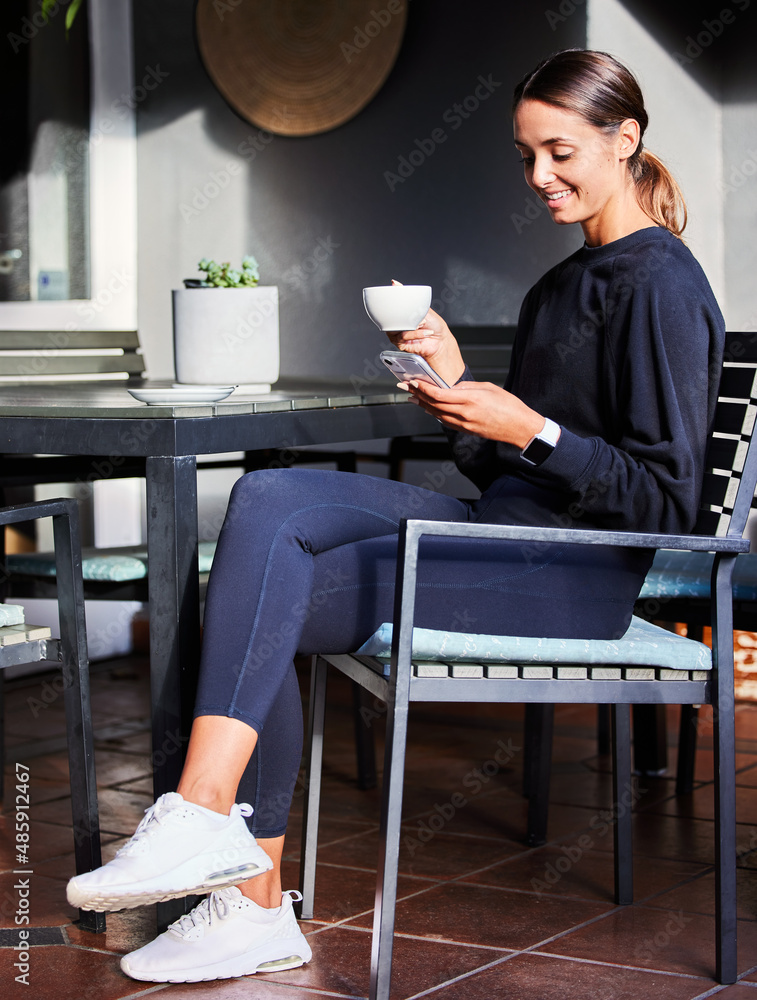 Enjoying a coffee break. Shot of a woman using her cellphone while sitting outside with a cup of cof