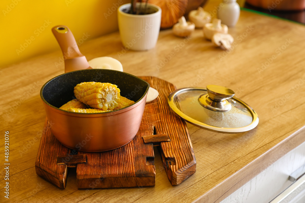 Sauce pan with corn cobs on wooden table