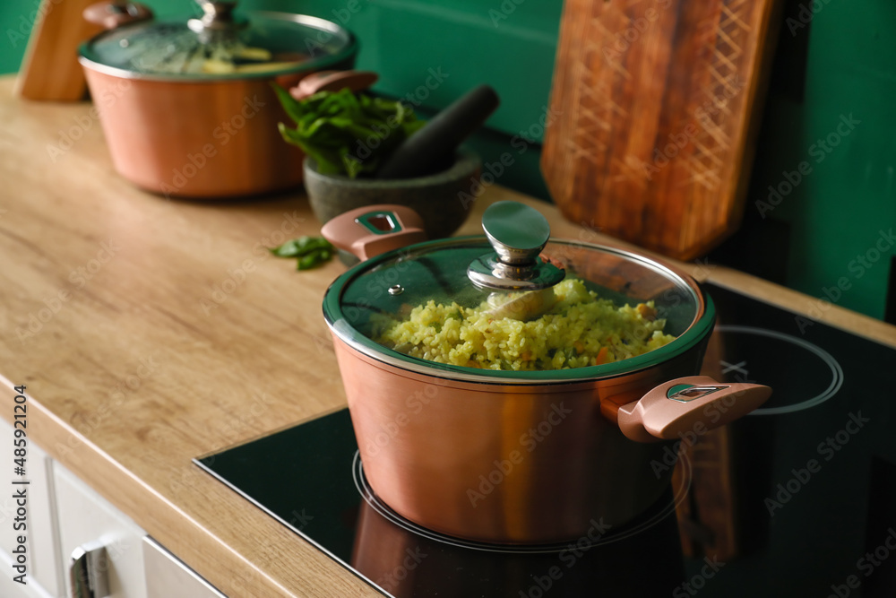 Cooking pot with pilaf on stove near color wall, closeup