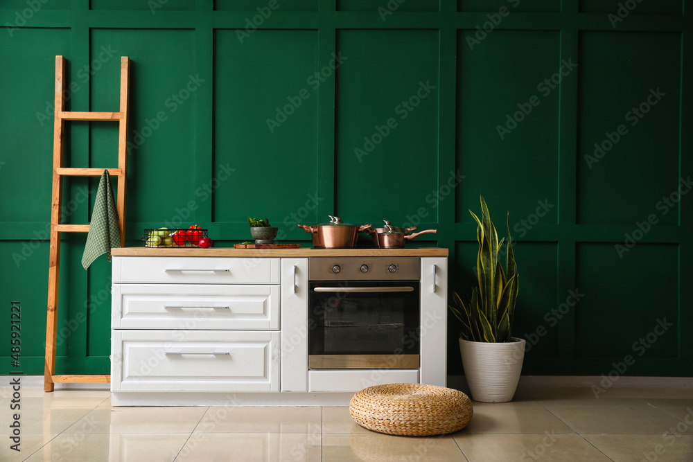 Interior of modern kitchen with white furniture near color wall and pouf on floor