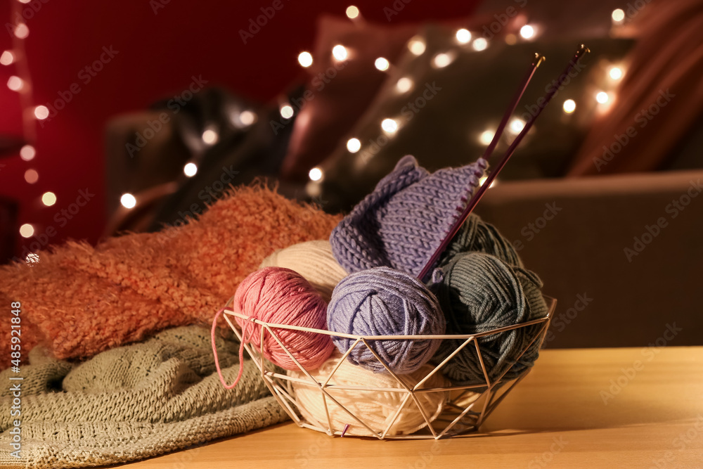 Basket with knitting yarn and needles on wooden table