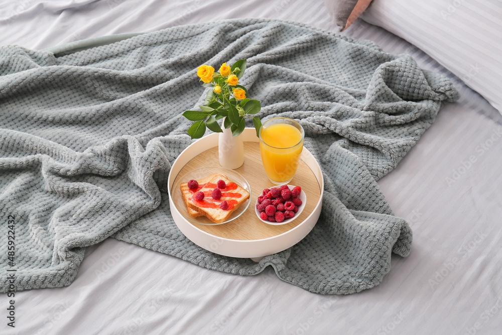 Tray with breakfast and vase with flowers on soft plaid