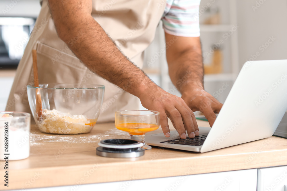 Handsome man using laptop while cooking in kitchen, closeup