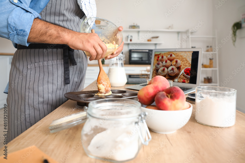 一名年轻男子在厨房观看视频教程时正在准备桃子松饼