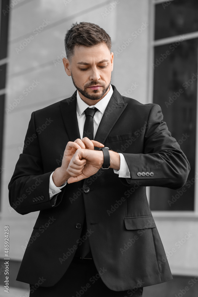 Stylish businessman using smartwatch near office building