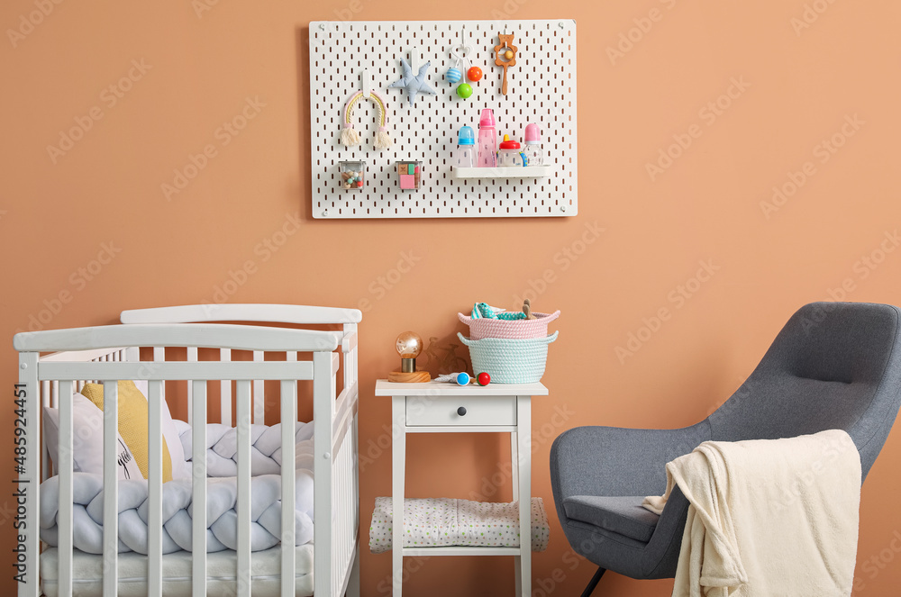 Interior of stylish childrens bedroom with crib and hanging pegboard on beige wall