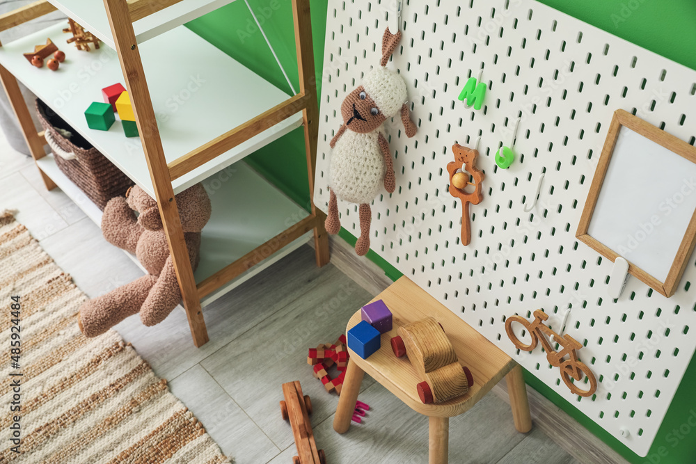 Shelving unit with toys and pegboard on stool near green wall