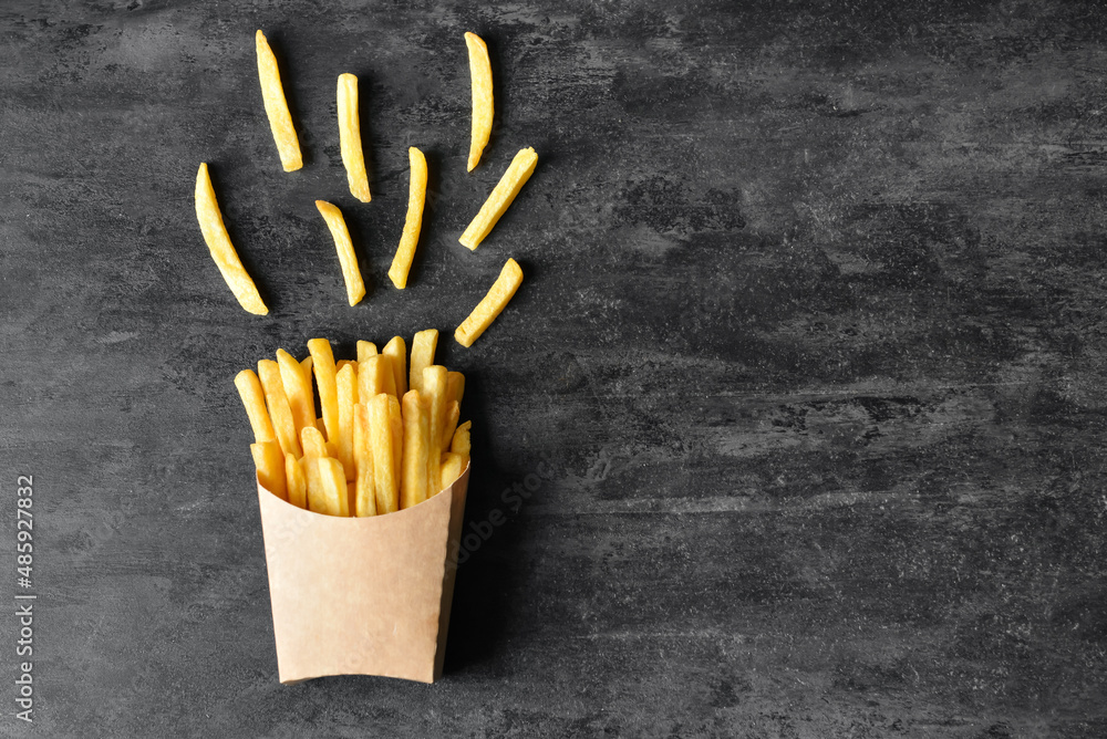 Paper box with tasty french fries on black background