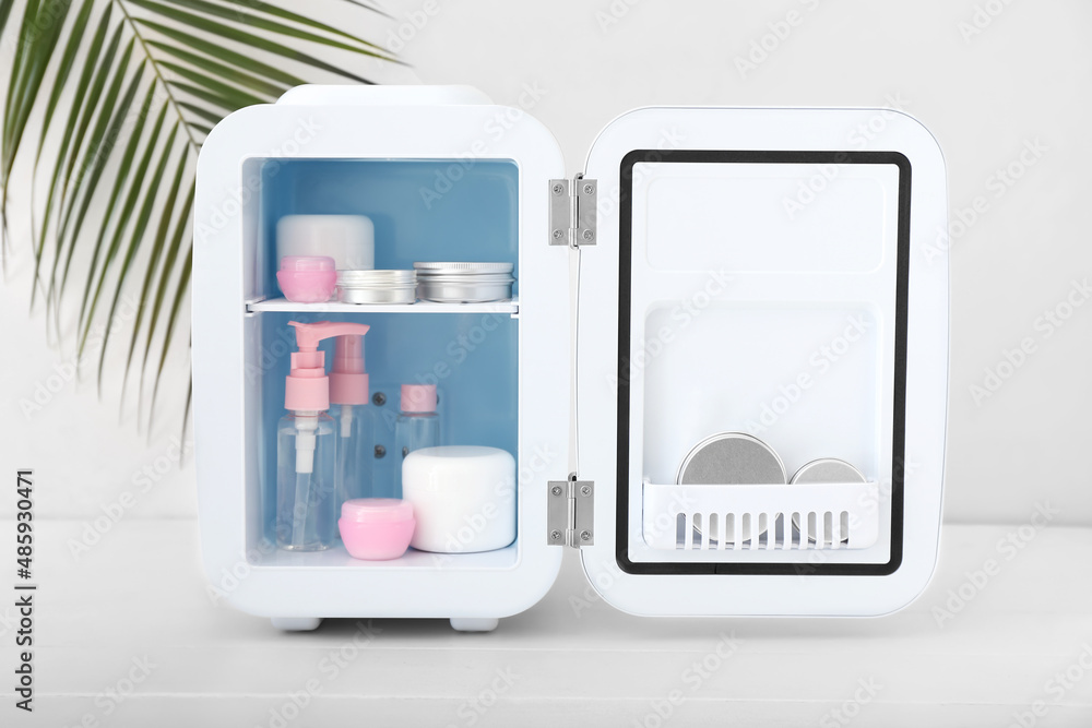 Small refrigerator with cosmetic products on light table